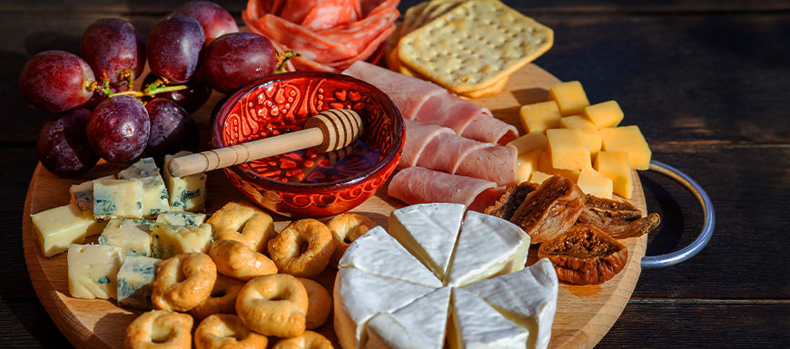 Circular charcuterie board with honey, cheeses, fruits, and nuts.